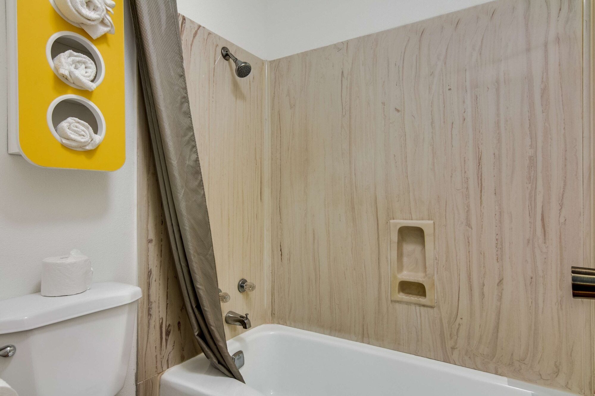 A bathroom with a wooden wall, a bathtub, a toilet, and a towel rack with three towels.