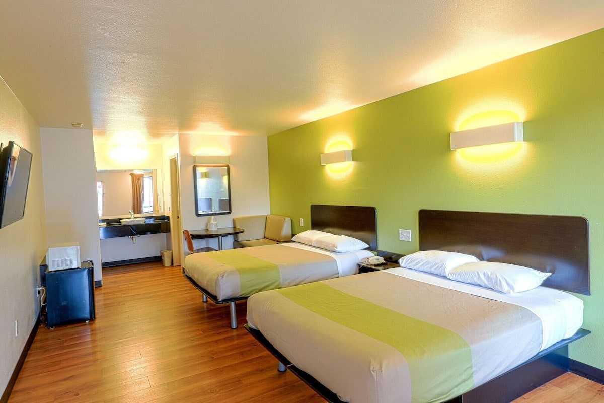 A hotel room with two beds, a small desk, a mirror, and a bathroom.