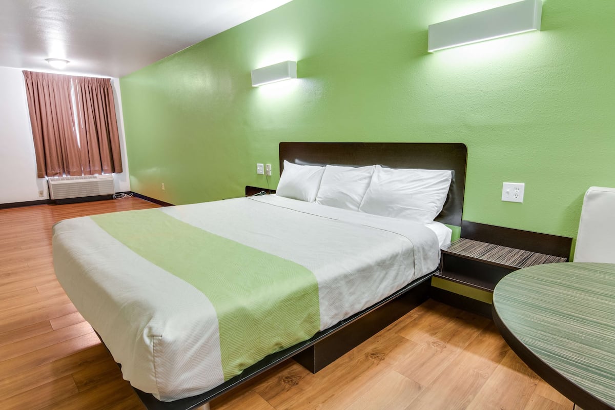 A hotel room with a bed, a bedside table, a chair, and a green wall.