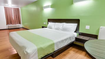 Habitación de hotel con una cama, una mesita de noche, una silla y una pared verde.