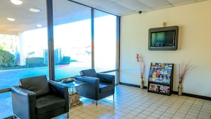 Un espace d’accueil comprenant deux fauteuils en cuir noir, une petite table avec un récipient, un sol carrelé, un téléviseur fixé au mur et un présentoir à magazines contenant diverses publications.