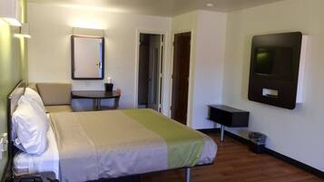 Habitación de hotel con cama, mesita de noche, lámpara, televisión y una pequeña mesa con una silla.