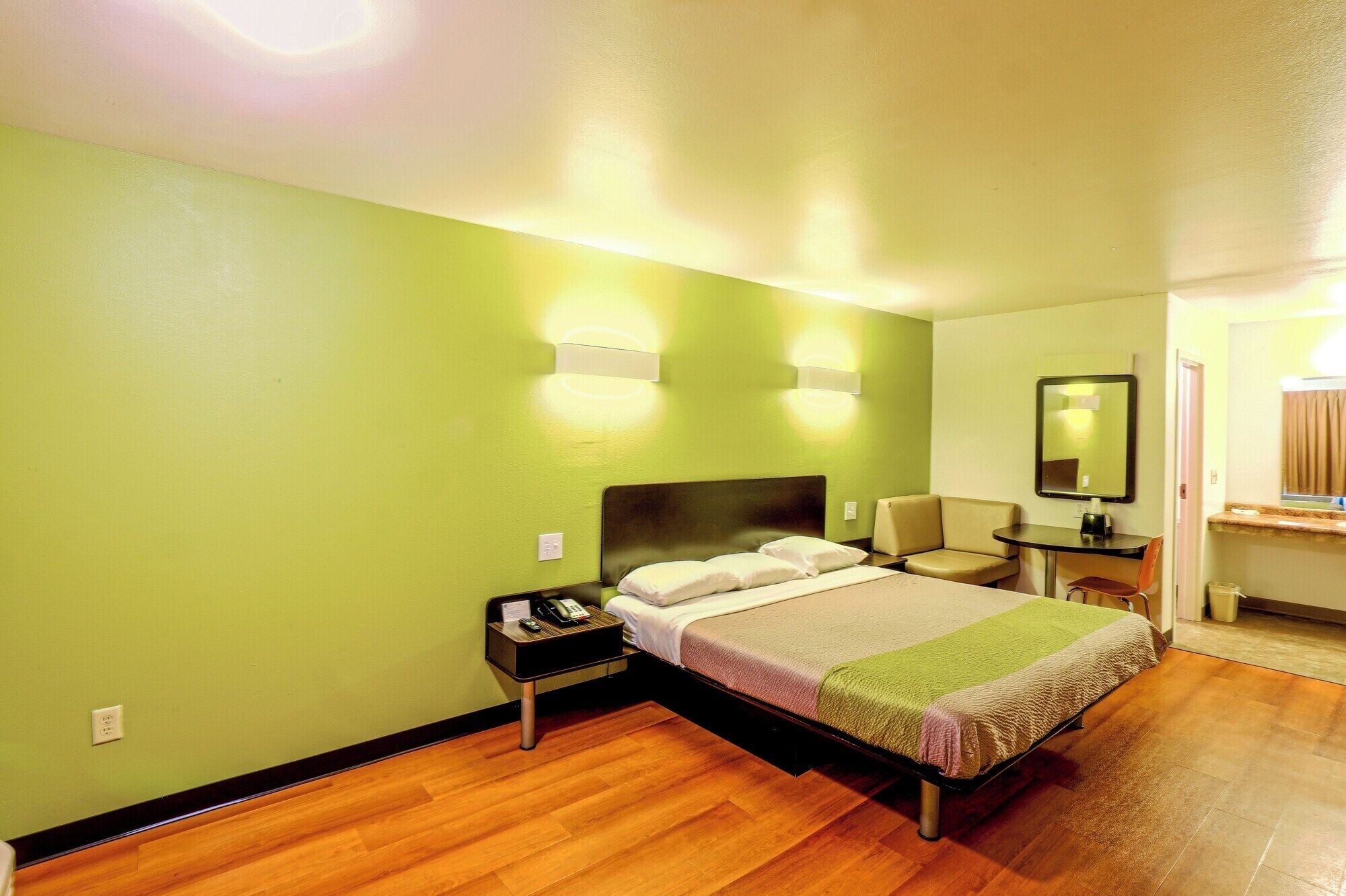 A hotel room with a bed, bedside table, chair, and a small desk with a mirror.