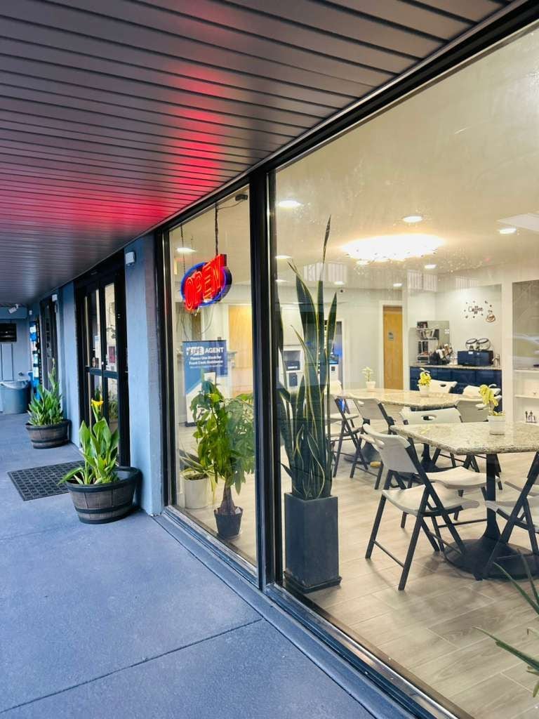 En moderne bygning med en glasfacade, et synligt 'OPEN'-skilt og et spiseområde med borde og stole.