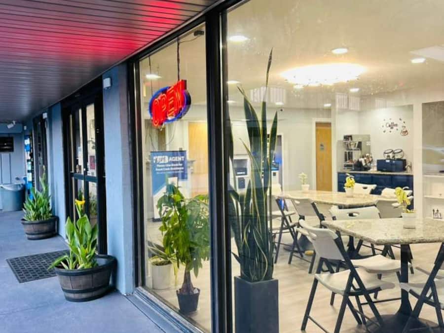 A modern building with a glass facade, a visible 'OPEN' sign, and a dining area with tables and chairs.