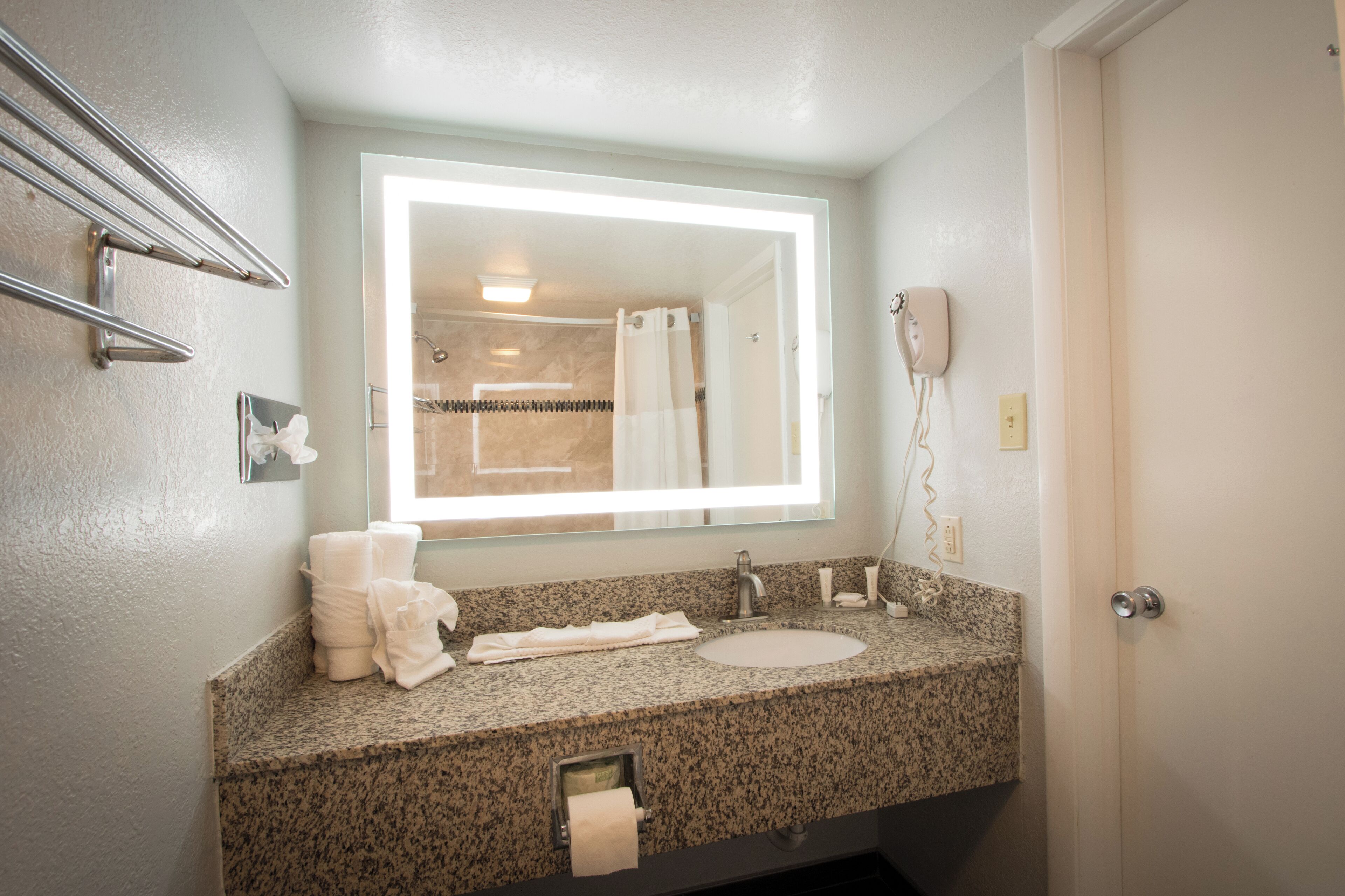 Un baño con encimera de granito, un lavabo, un espejo, toallero y una ducha a simple vista.