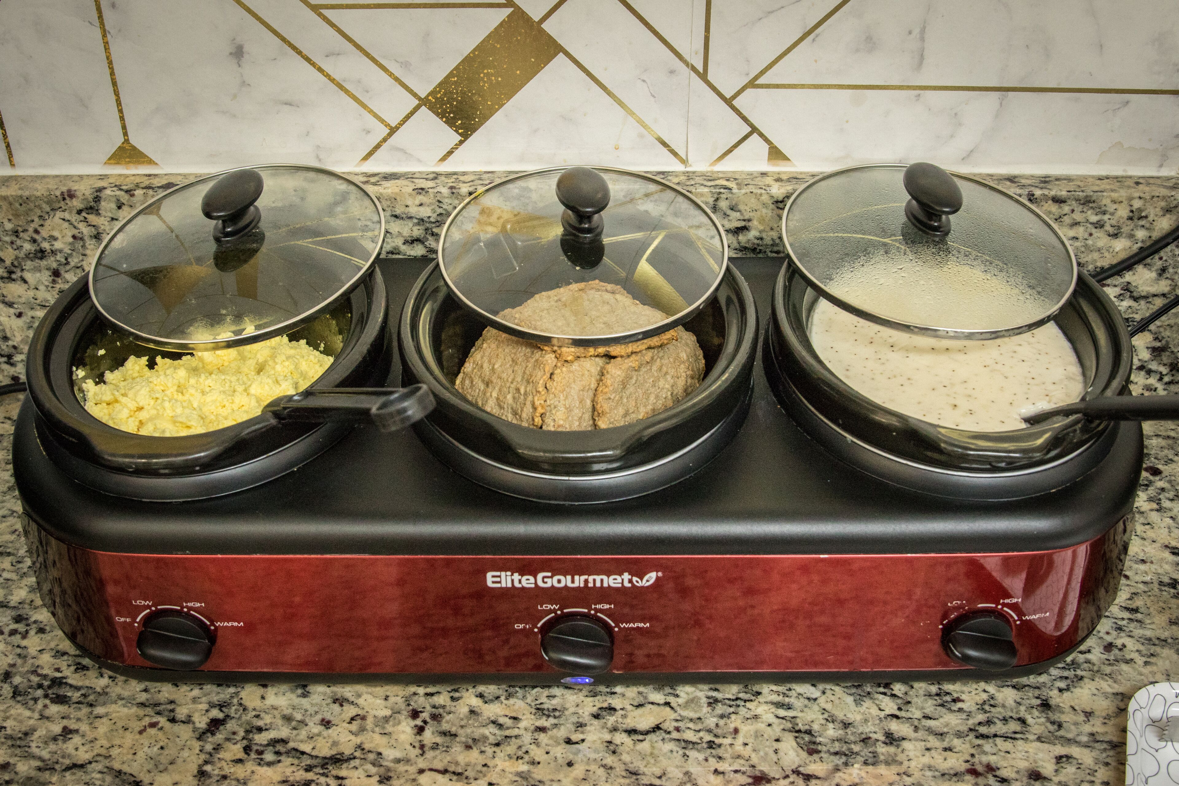 A three-compartment slow cooker with lids, labeled "Elite Gourmet," on a granite countertop.