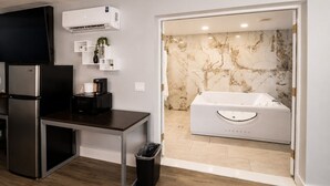 A compact kitchen with a refrigerator, microwave, and coffee maker, a trash bin, and a bathroom with a marble wall and a bathtub. - Envi Boutique Hotel Henderson-Evansville South (Henderson)