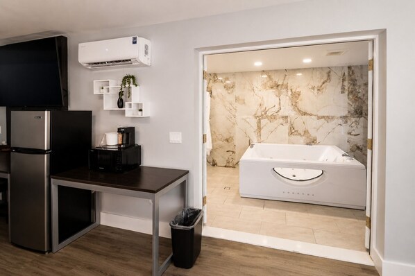 A compact kitchen with a refrigerator, microwave, and coffee maker, a trash bin, and a bathroom with a marble wall and a bathtub. - Envi Boutique Hotel Henderson-Evansville South (Henderson)