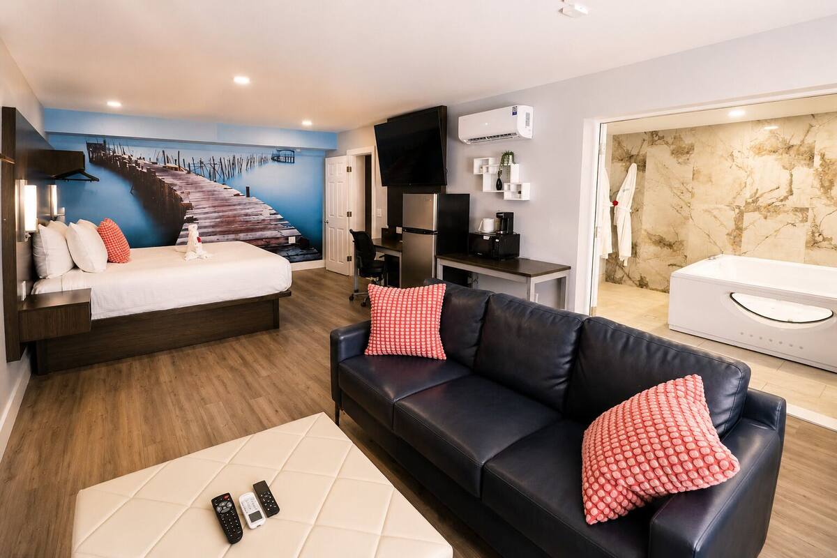 A modern hotel room with a bed, a black leather sofa, a coffee table, a TV, and a marble wall.