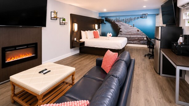A modern living room with a fireplace, a sofa, a bed, and a kitchen area. - Envi Boutique Hotel Henderson-Evansville South (Henderson)
