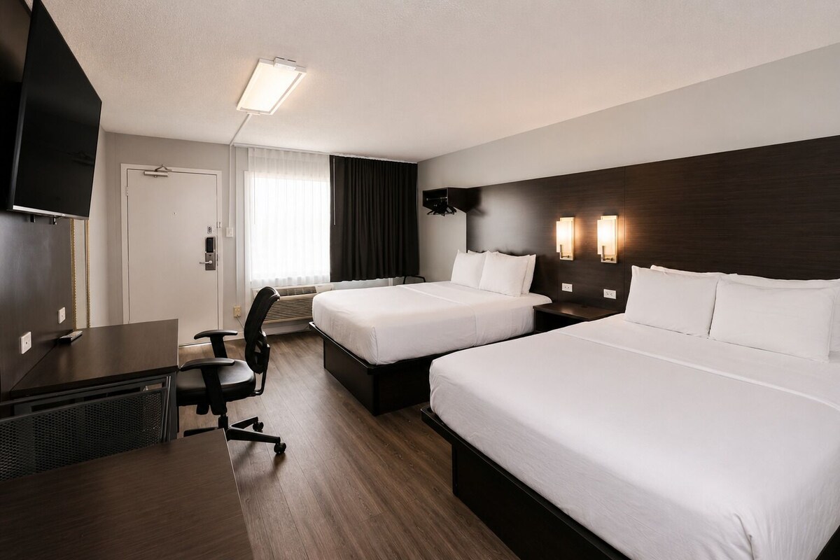 A hotel room with two beds, a desk, a chair, a TV, and a window with curtains.