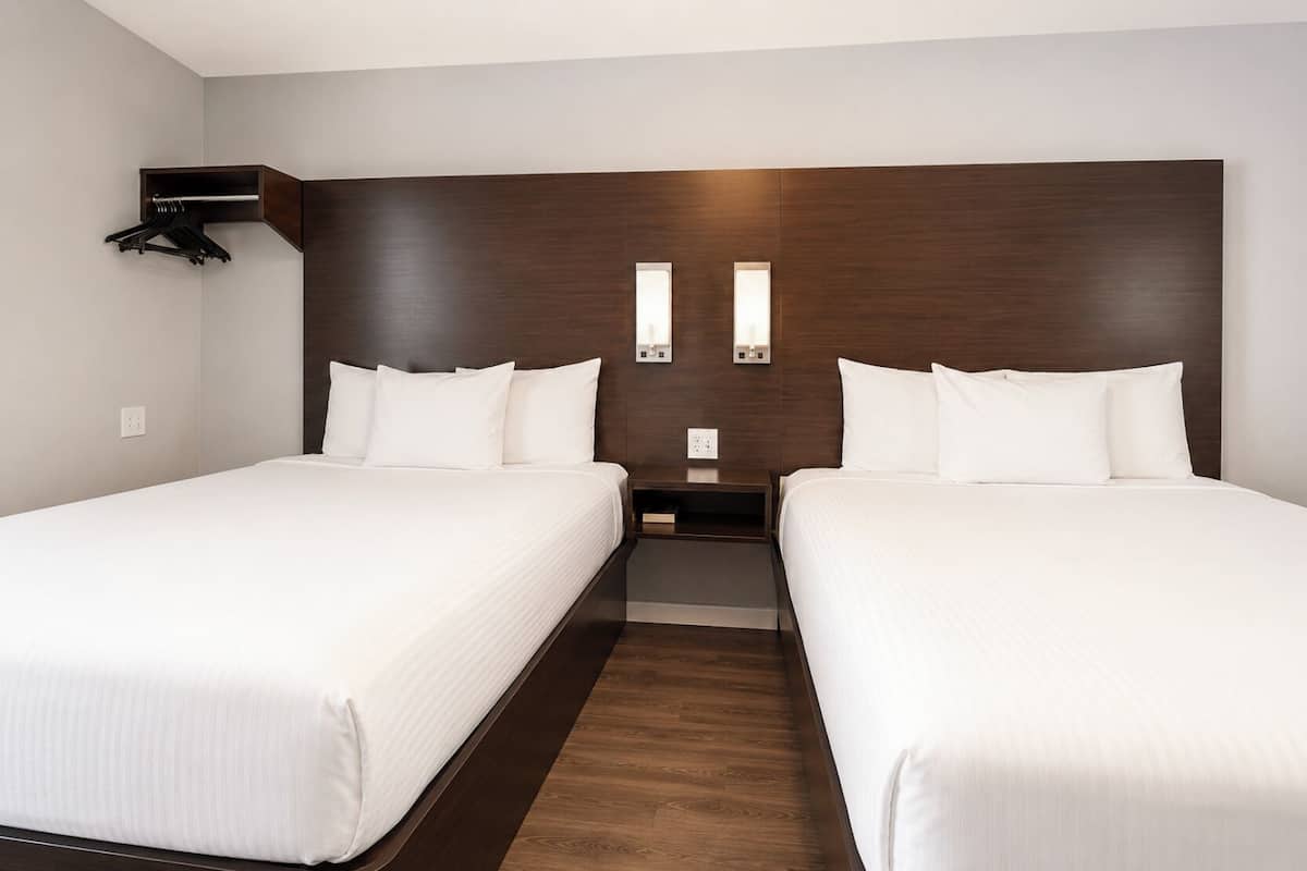 A hotel room with two single beds, a dark wood headboard, bedside tables, and a wall-mounted light fixture.