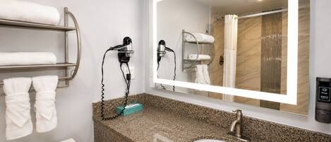 Un baño con encimera de granito, un lavabo, un inodoro, toallero, secador de pelo y un espejo.