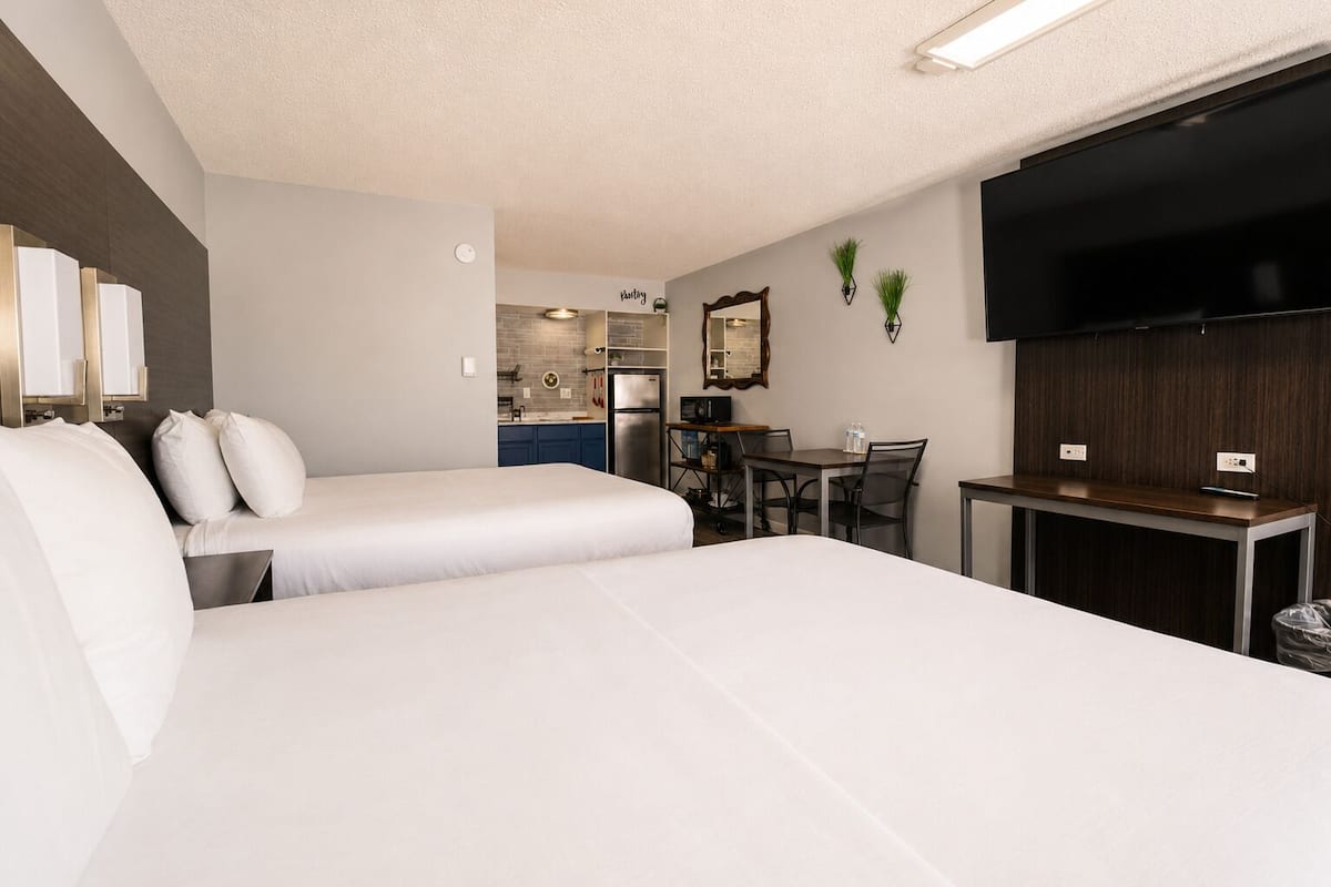 A hotel room with two beds, a kitchenette, a dining table, and a TV.