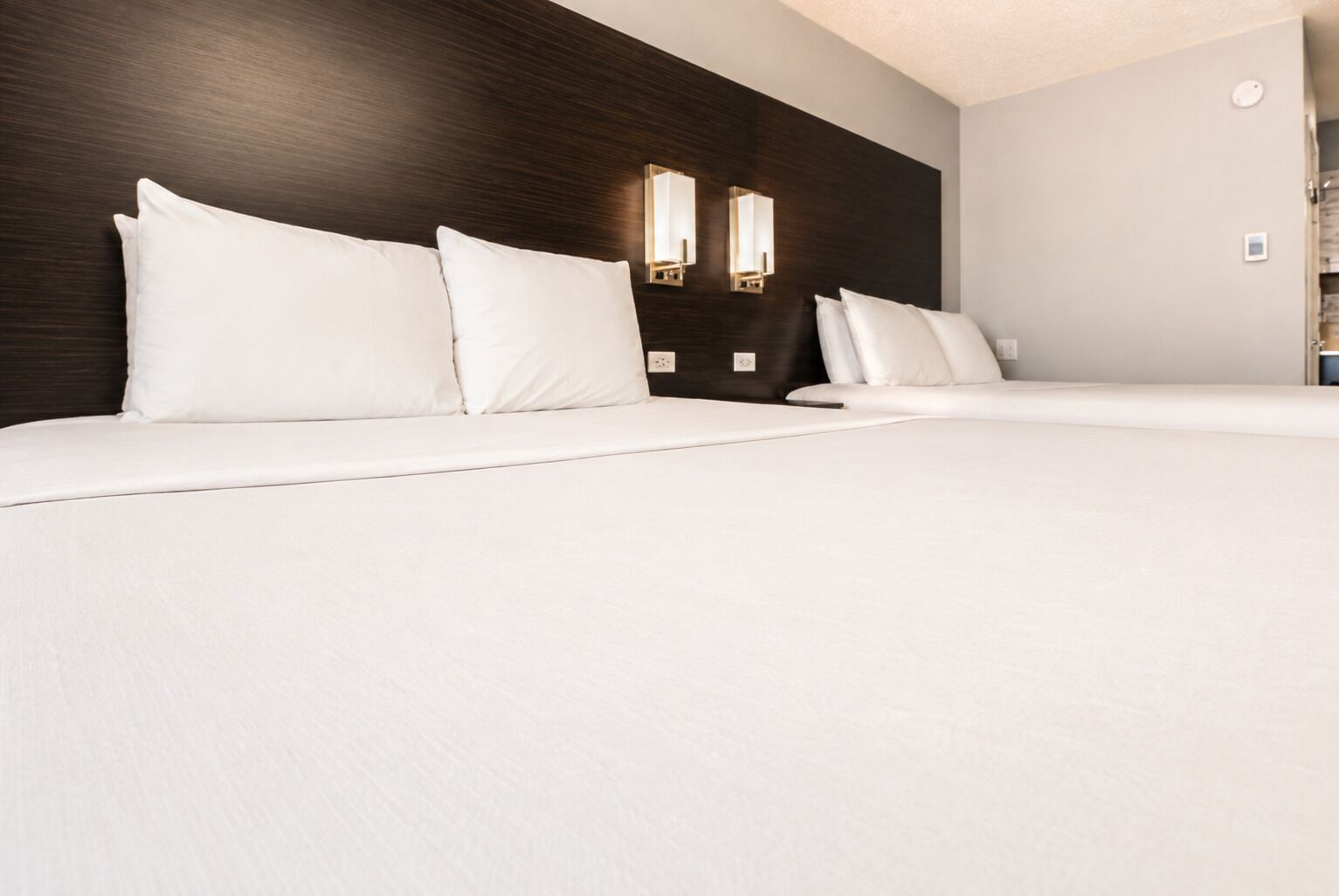 A hotel room with a large bed, a dark wood headboard, and two wall-mounted light fixtures.