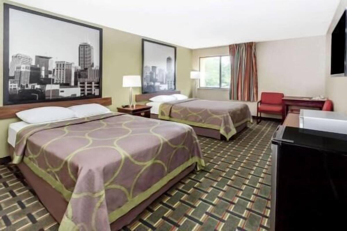 A hotel room with two beds, a desk, a chair, and a large cityscape painting on the wall.