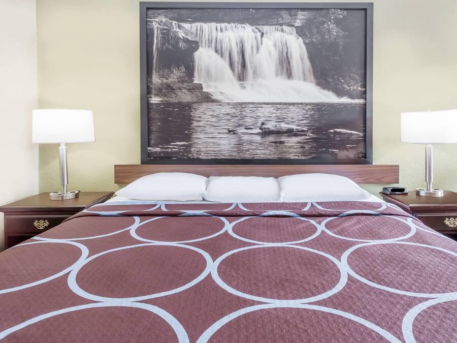 A hotel room with a bed, two bedside tables, a nightstand, a large framed waterfall photograph on the wall, and two lamps.