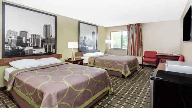 A hotel room with two beds, a desk, a chair, a TV, and a cityscape painting on the wall. - Super 8 by Wyndham Logansport (Logansport)