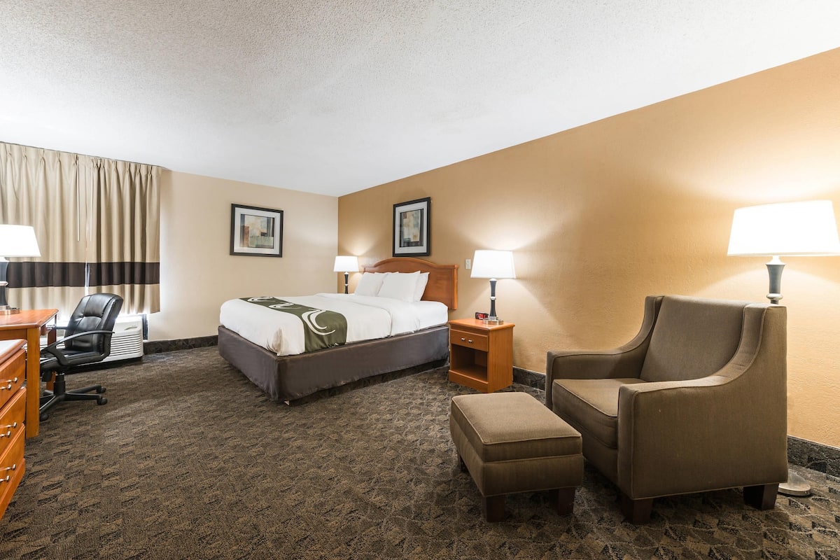 A hotel room with a bed, two bedside tables with lamps, a chair, a desk, and a dresser.