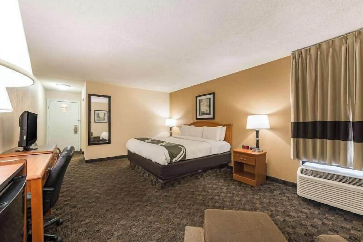 A hotel room with a bed, bedside tables, a desk, a chair, a television, and a window with curtains.