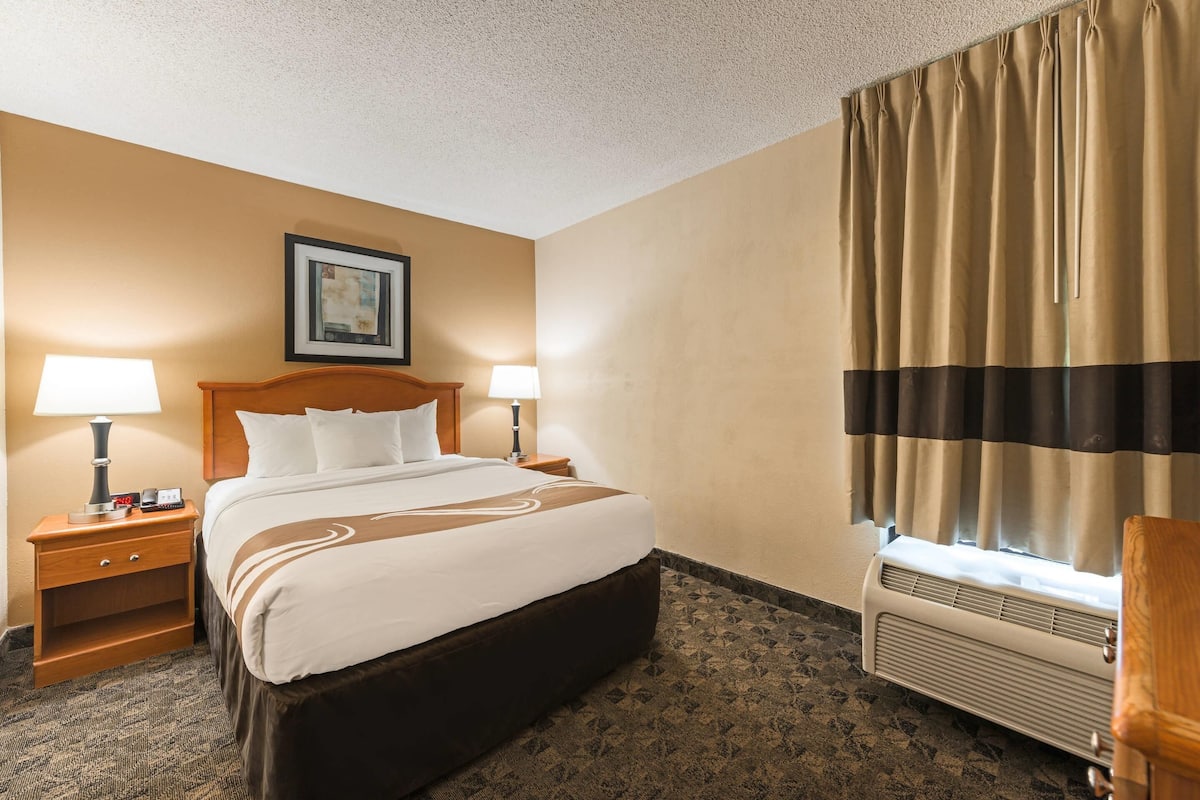 A hotel room with a large bed, two bedside tables with lamps, a framed picture on the wall, and a window with curtains.