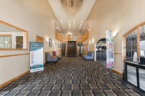 A hotel lobby with a check-in counter, seating area, staircase, and a reception desk.