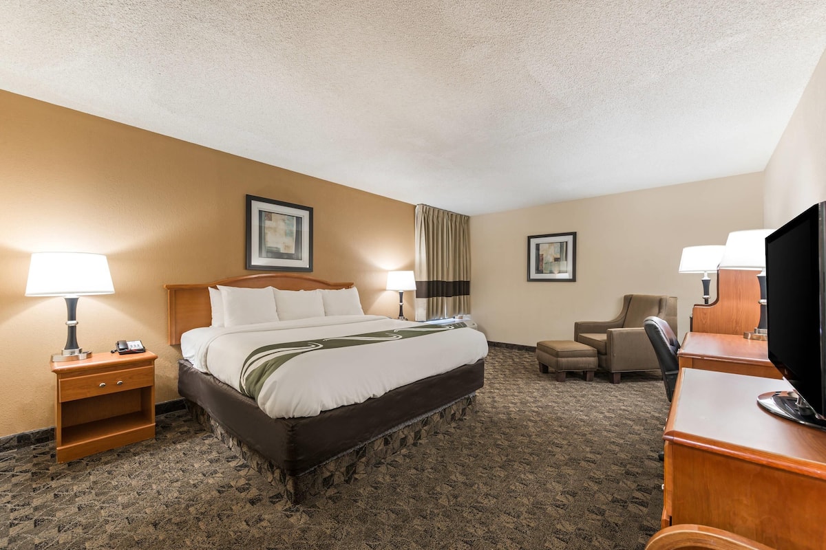 A hotel room with a bed, bedside lamps, a desk with a television, a chair, and a carpeted floor.