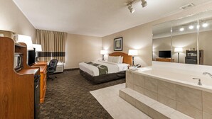 A hotel room with a bed, desk, chair, and a large bathroom with a bathtub and mirror. - Quality Inn & Suites Portage Central (Portage)