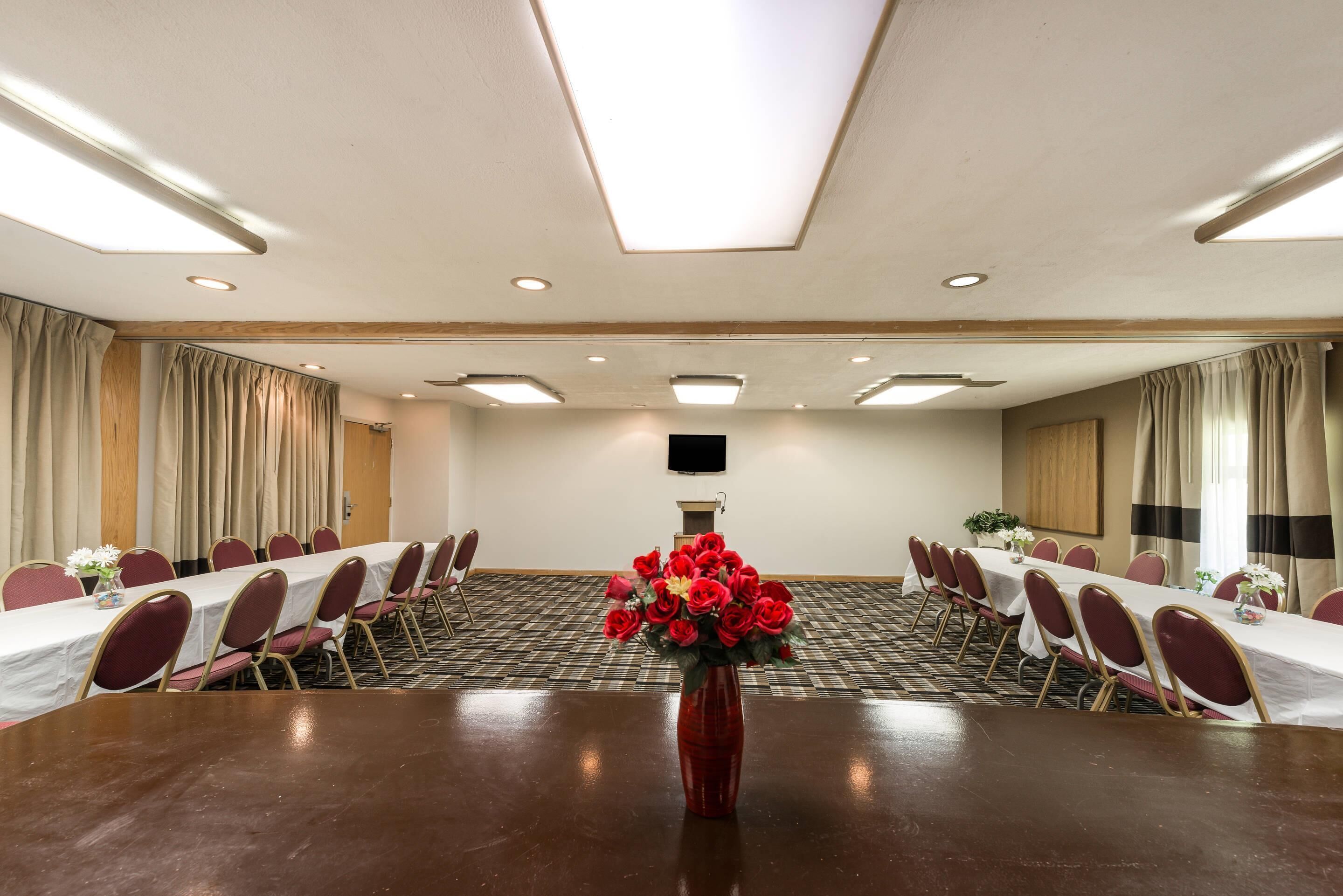 Un salón de conferencias con una mesa larga, sillas, un florero rojo con flores y un televisor de pantalla plana en la pared.