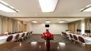 Un salón de conferencias con una mesa larga, sillas, un florero rojo con flores y un televisor de pantalla plana en la pared.
