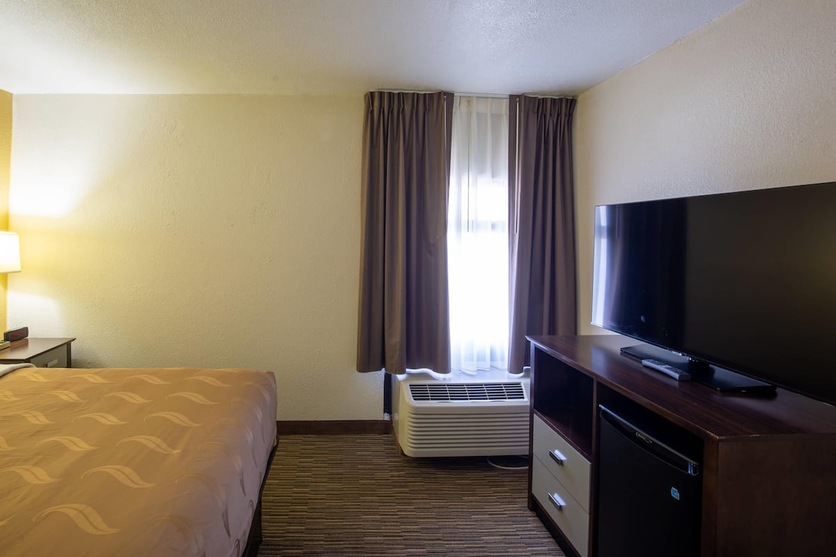 A hotel room with a bed, a television, a heater, and a window with curtains.
