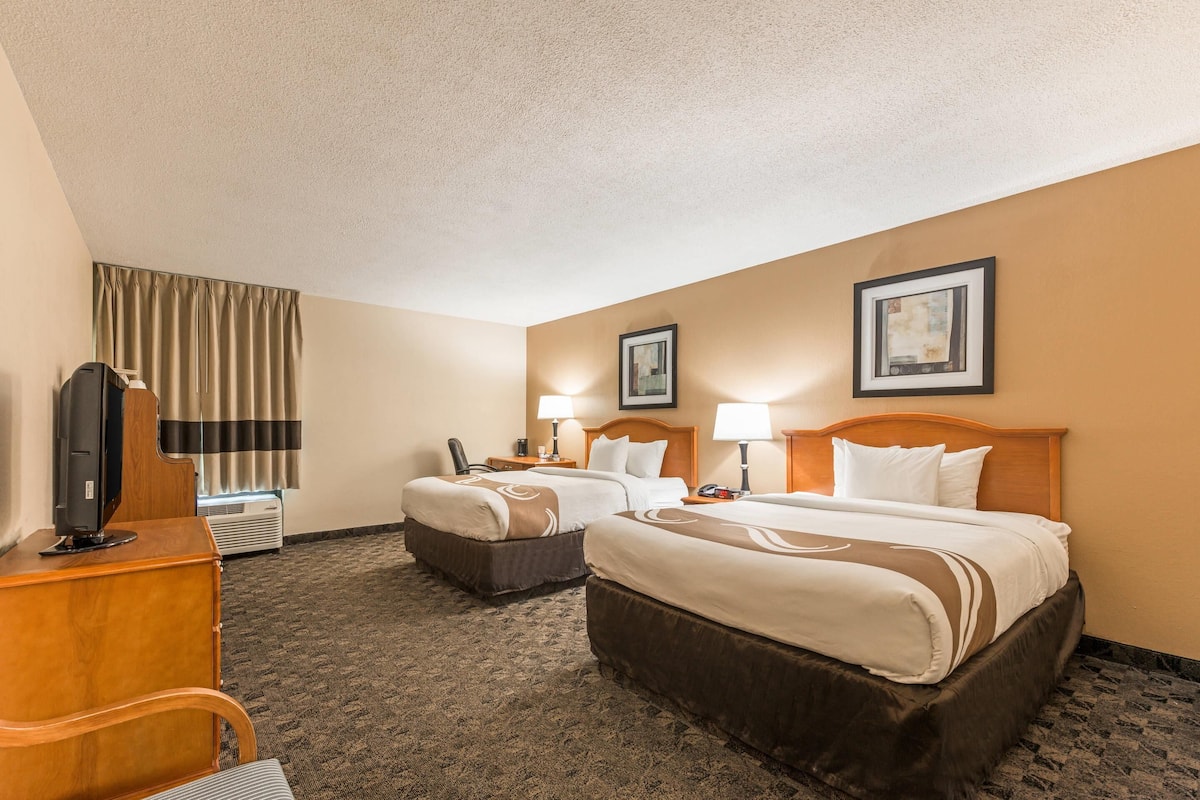 A hotel room with two beds, a desk with a TV, a chair, and two bedside lamps.