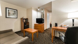 A hotel room with a sofa, a wooden desk, a television, a coffee maker, and a lamp. - Quality Inn & Suites Portage Central (Portage)