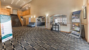 A hotel lobby with a check-in counter, a staircase, a seating area, and a patterned carpet. - Quality Inn & Suites Portage Central (Portage)