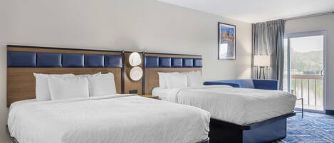 A hotel room with two beds, a large window with a view, a blue carpet, and a headboard with a clock.