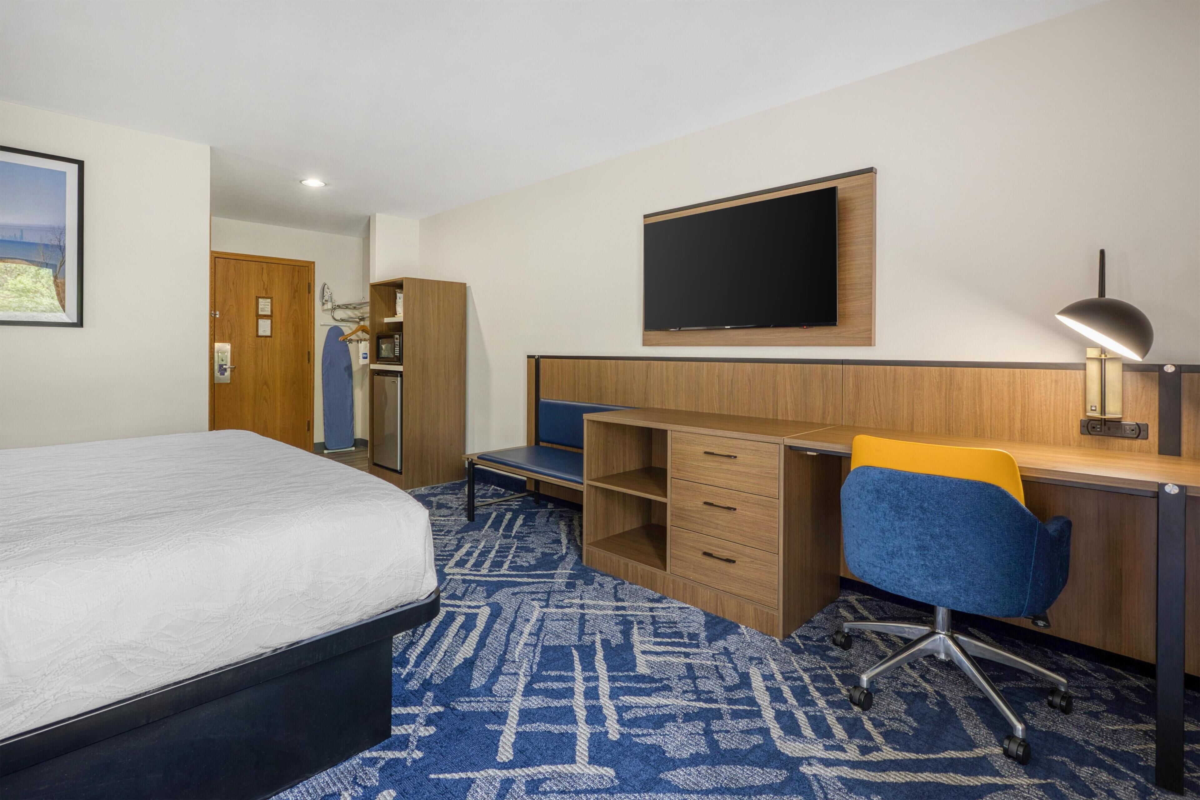Une chambre d’hôtel équipée d’un lit, d’un bureau, d’une chaise et d’un téléviseur fixé au mur.