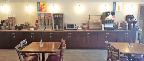 A breakfast bar with cereal, a microwave, and a coffee machine. There are wooden tables and chairs.