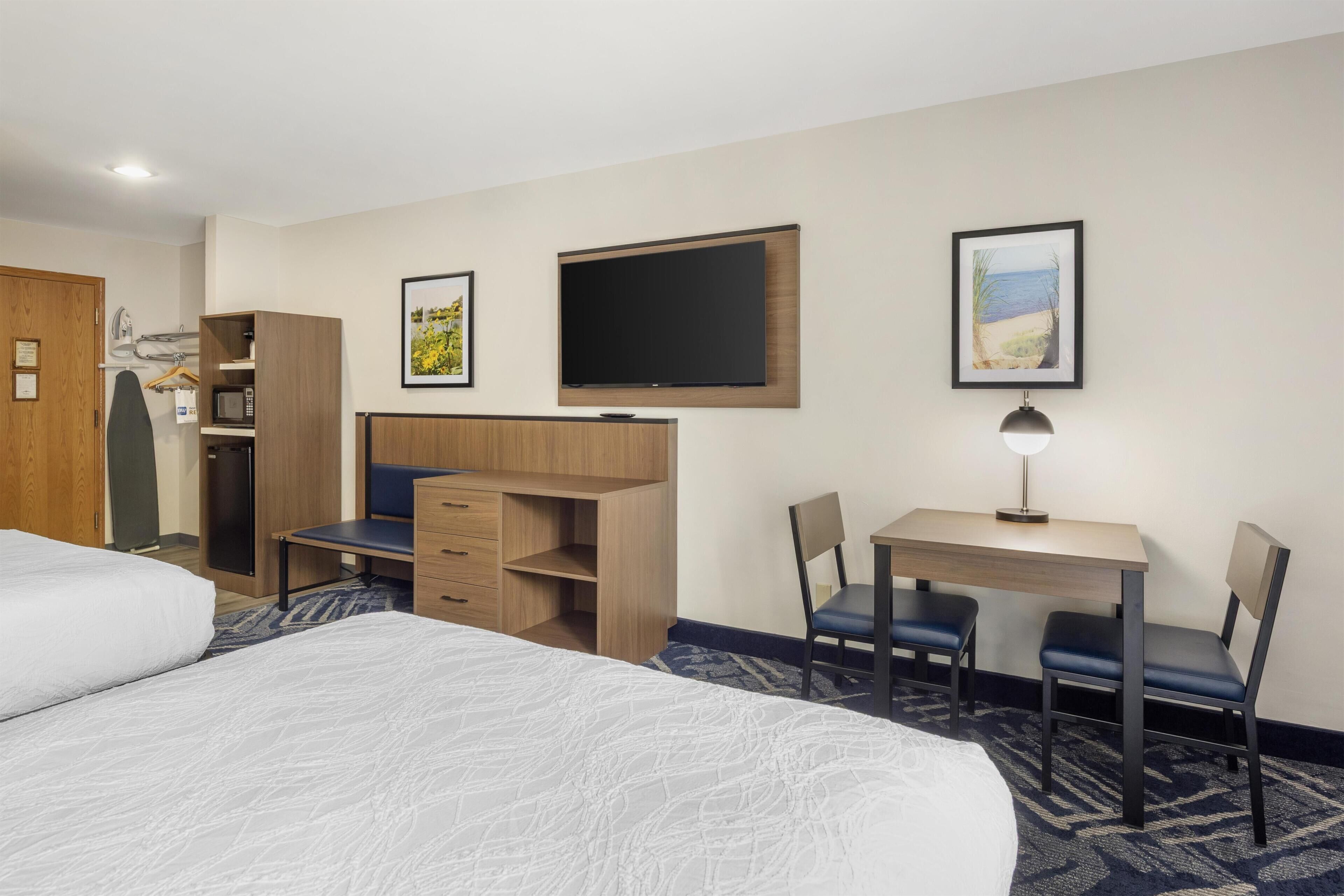 Habitación de hotel con cama, escritorio con dos sillas, televisor y armario.