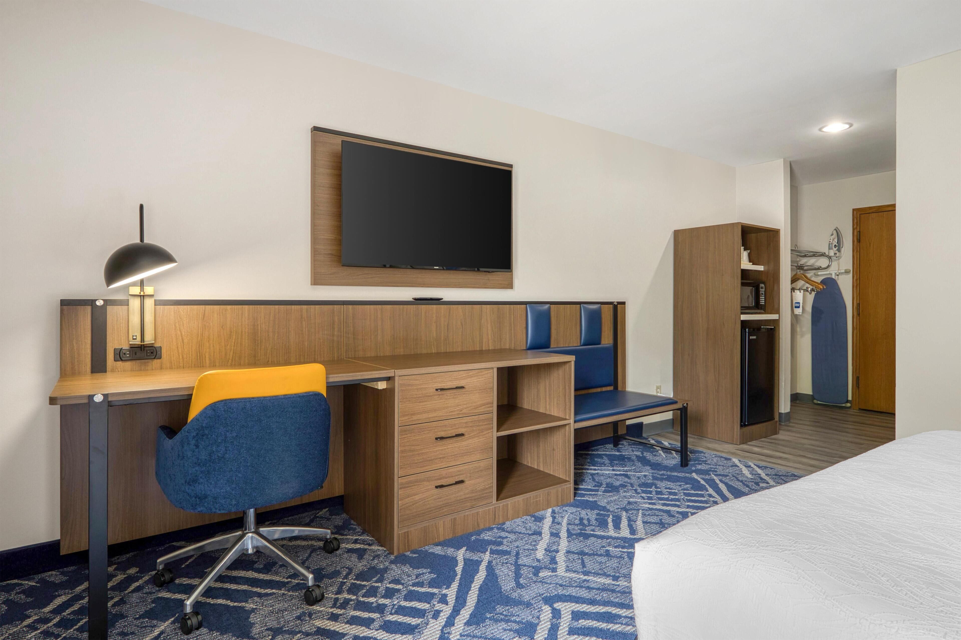 Een hotelkamer met een houten bureau, een blauwe stoel, een flatscreen televisie, een kledingkast en een bed.