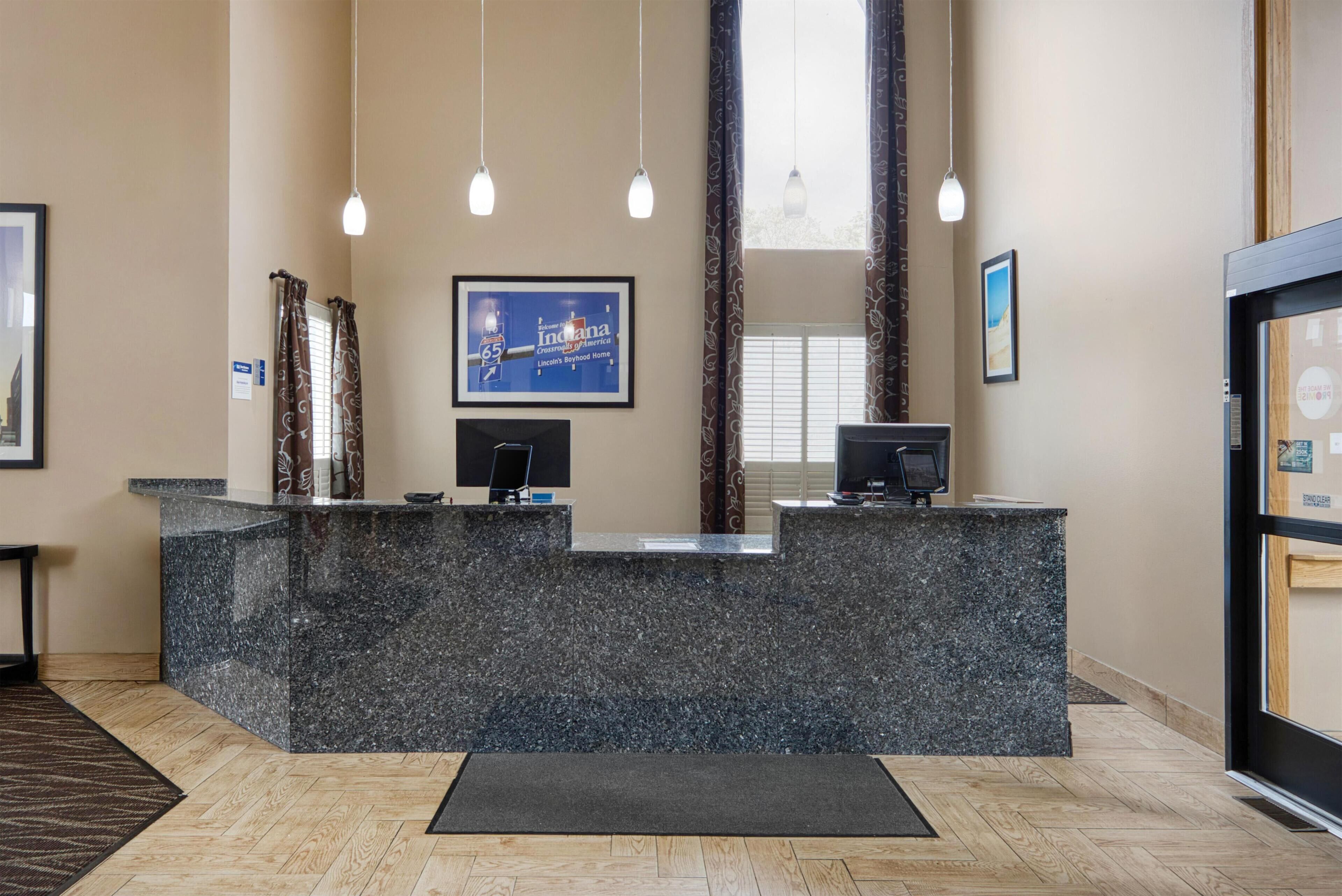 A reception desk with a stone counter, two monitors, and pendant lighting.