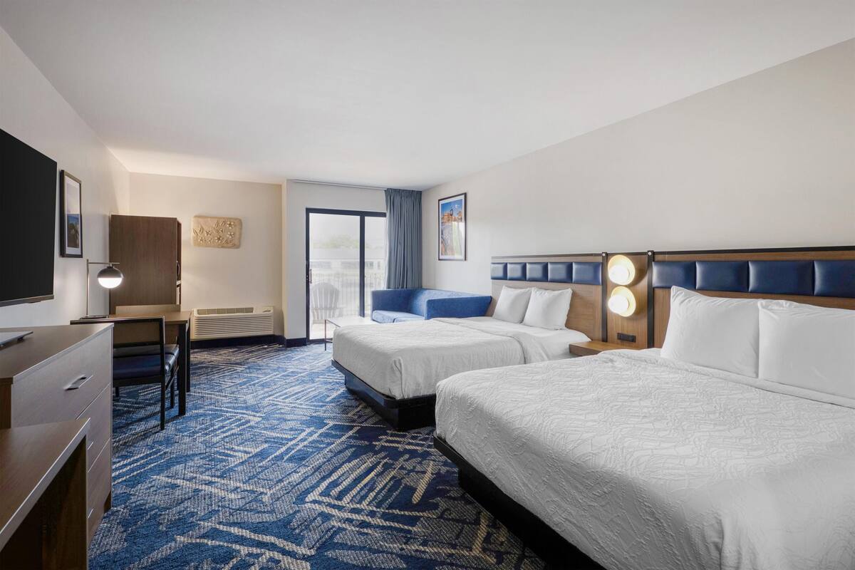 A hotel room with two beds, a desk, a chair, a TV, and a window with a view.