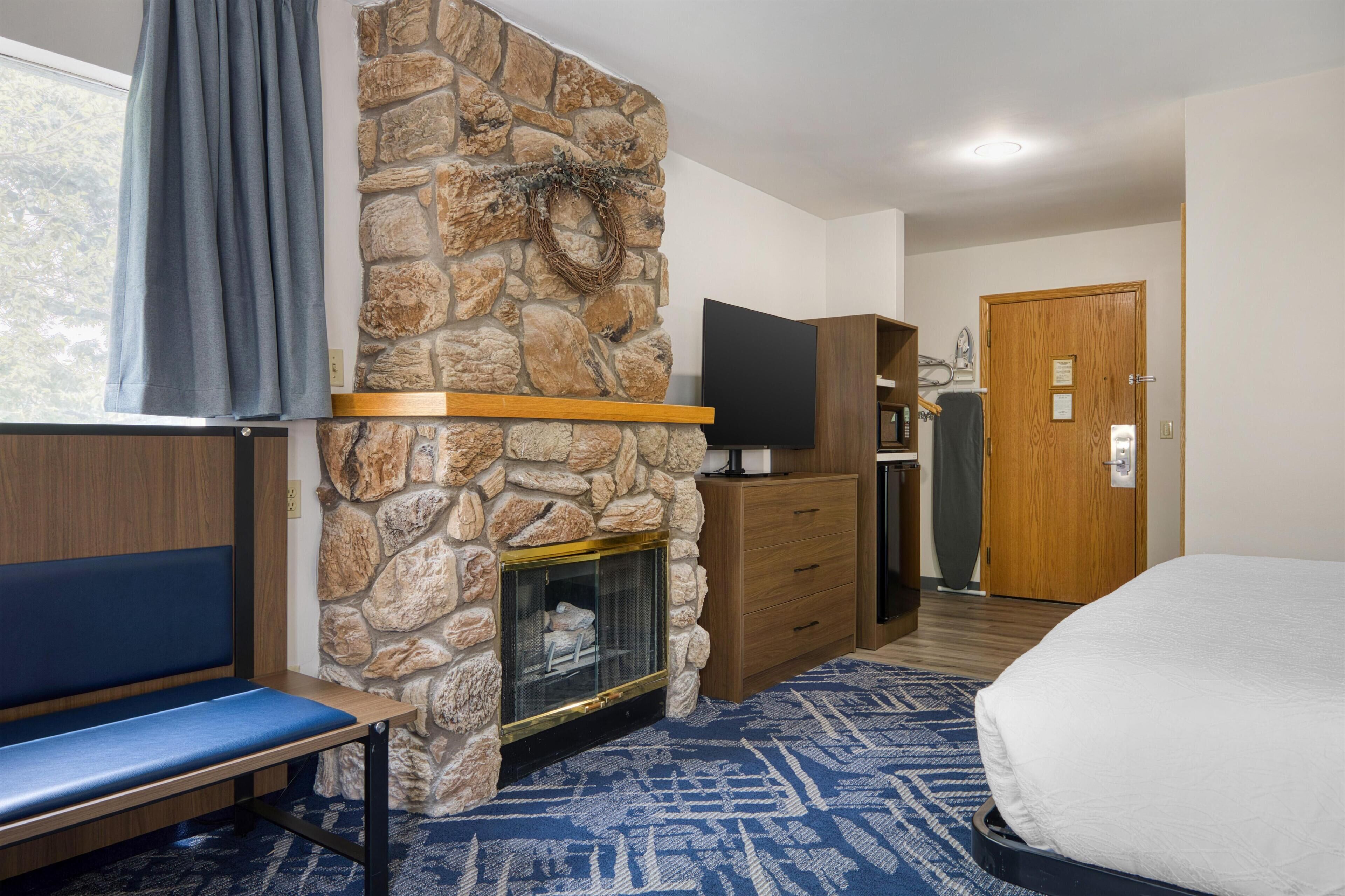 Ein Hotelzimmer mit Kamin aus Stein, einem Flachbildfernseher, einer hölzernen Bank, einem Bett und einer Tür.