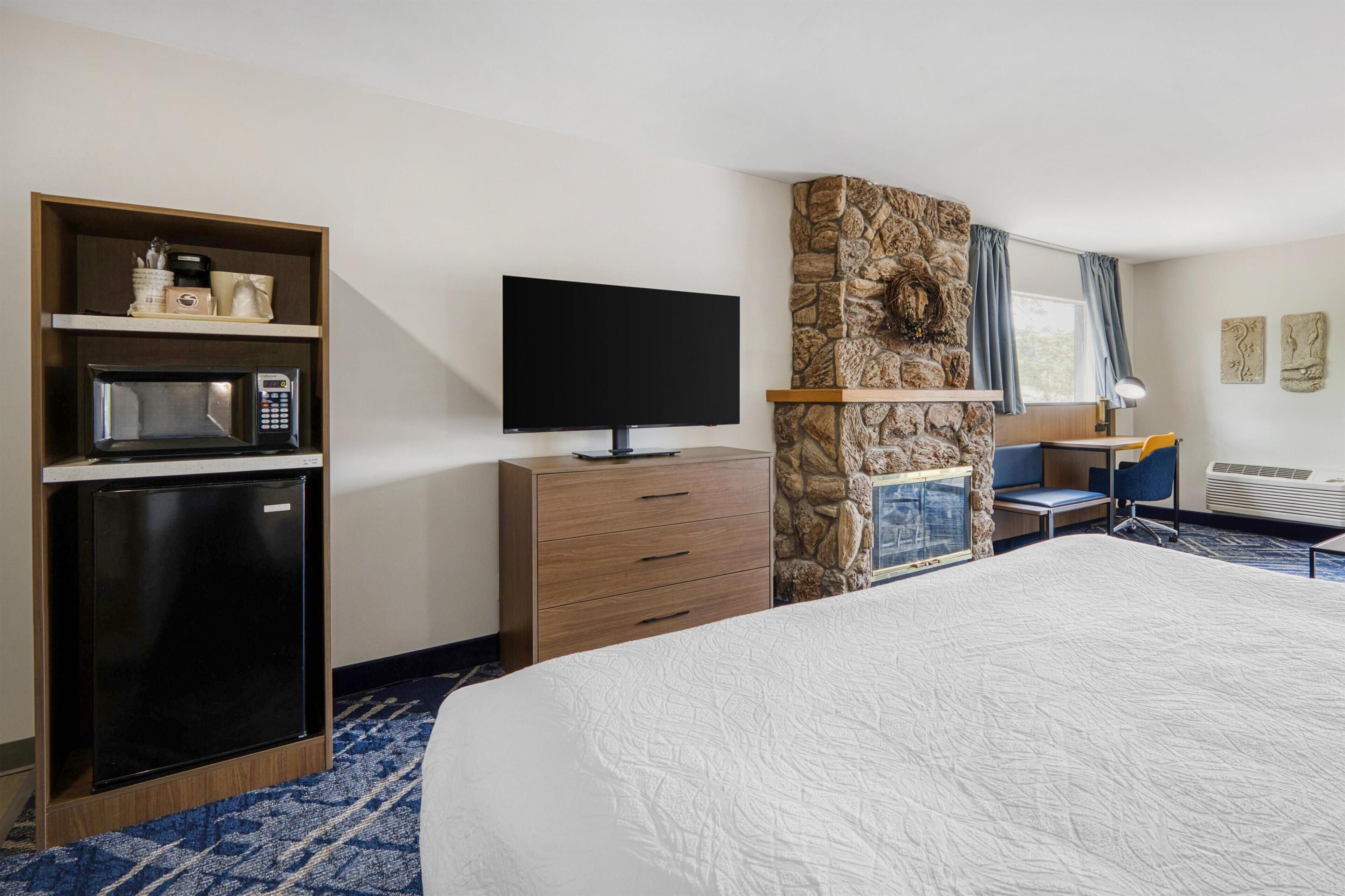 A hotel room with a bed, a TV, a microwave, a refrigerator, a desk, and a stone accent wall.