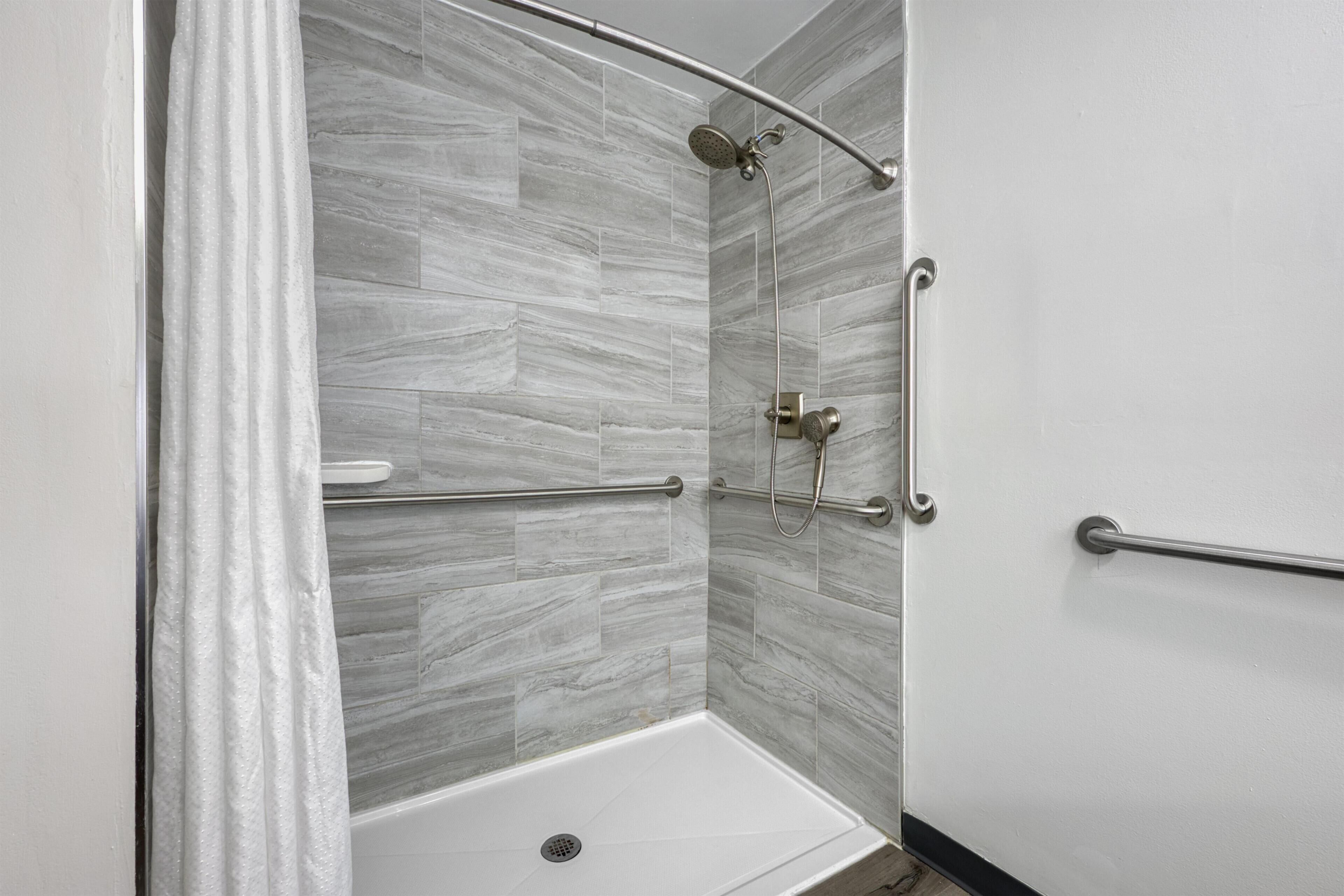 A shower with a glass door, a handrail, and a showerhead.
