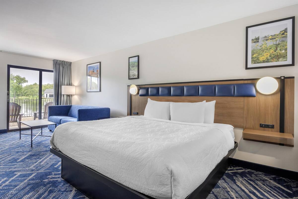 A hotel room with a large bed, a blue sofa, a small table, and a view through the window.