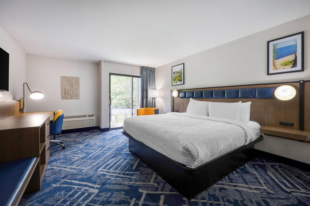 A hotel room with a bed, desk, chair, and a view of the outdoors.