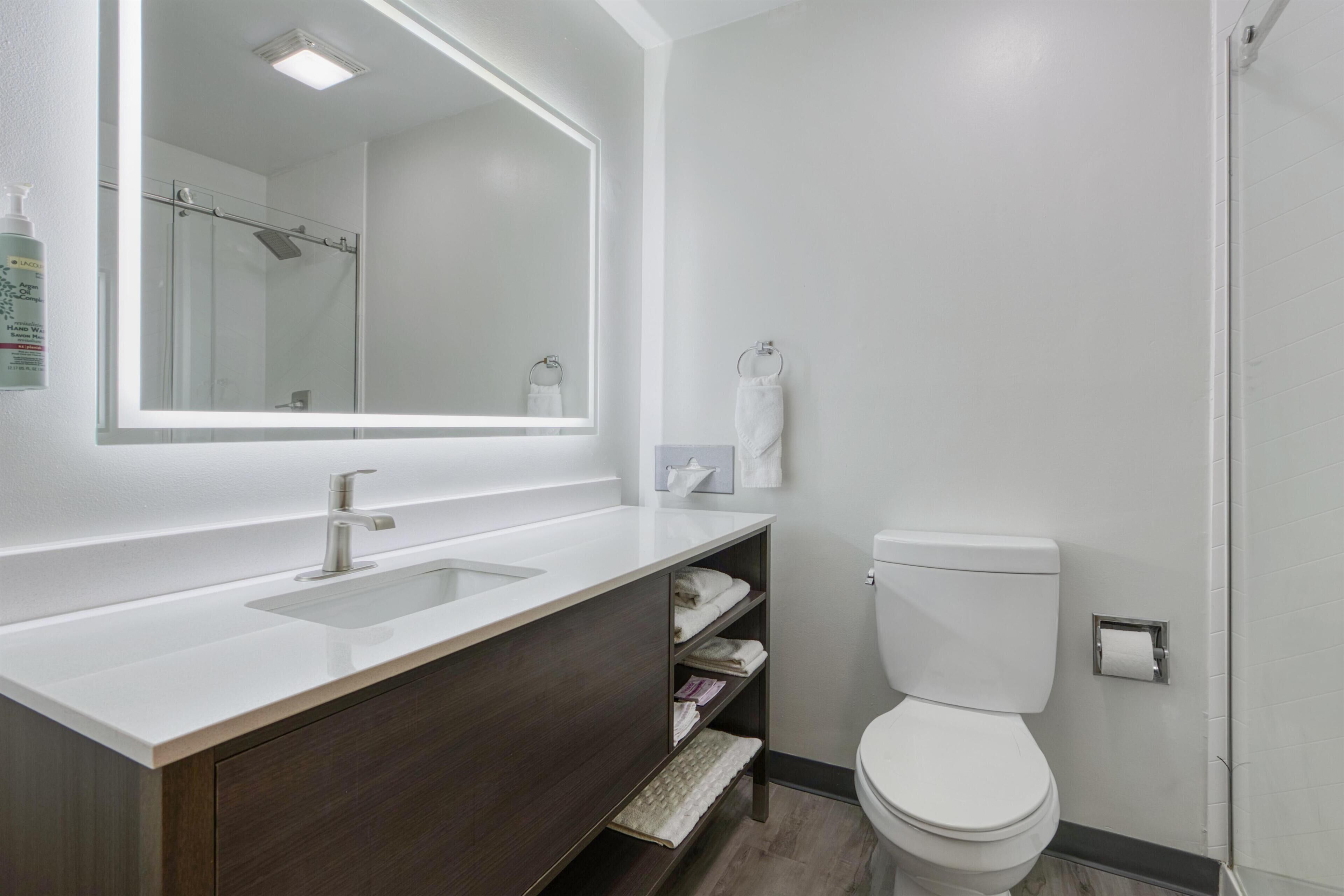 A modern bathroom with a large mirror, a white sink, a toilet, and a shower area.