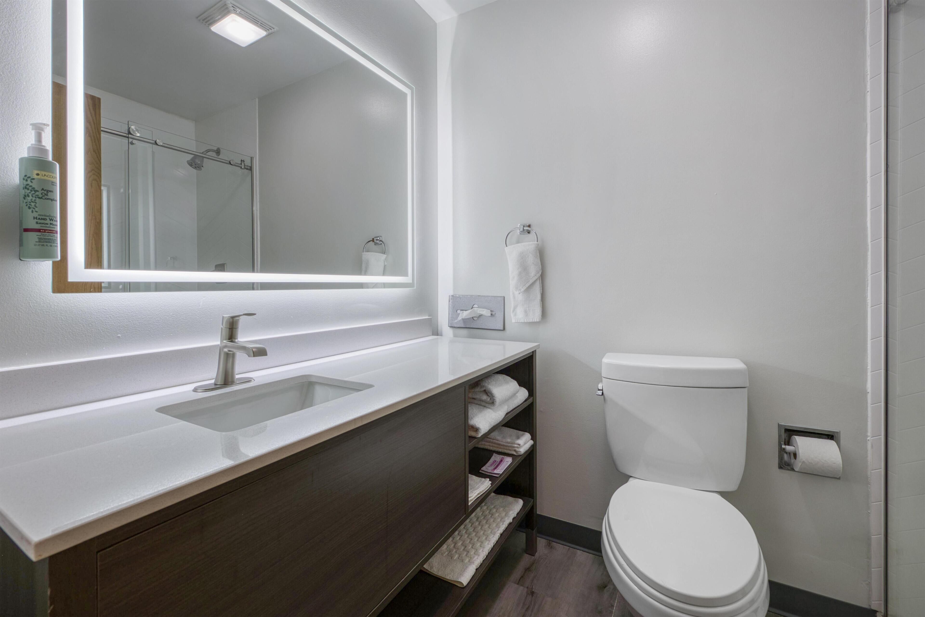 Un baño moderno con un espejo grande, un lavamanos, un inodoro y una ducha.