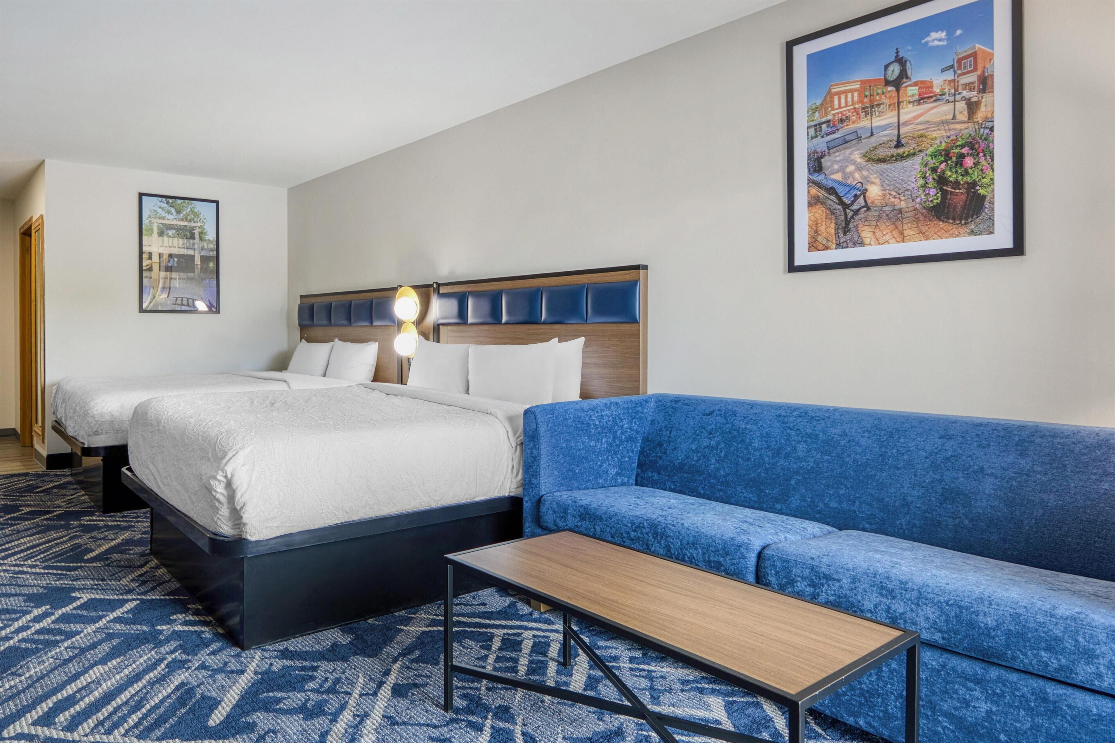 A hotel room with two beds, a blue sofa, a small table, and a framed picture on the wall.